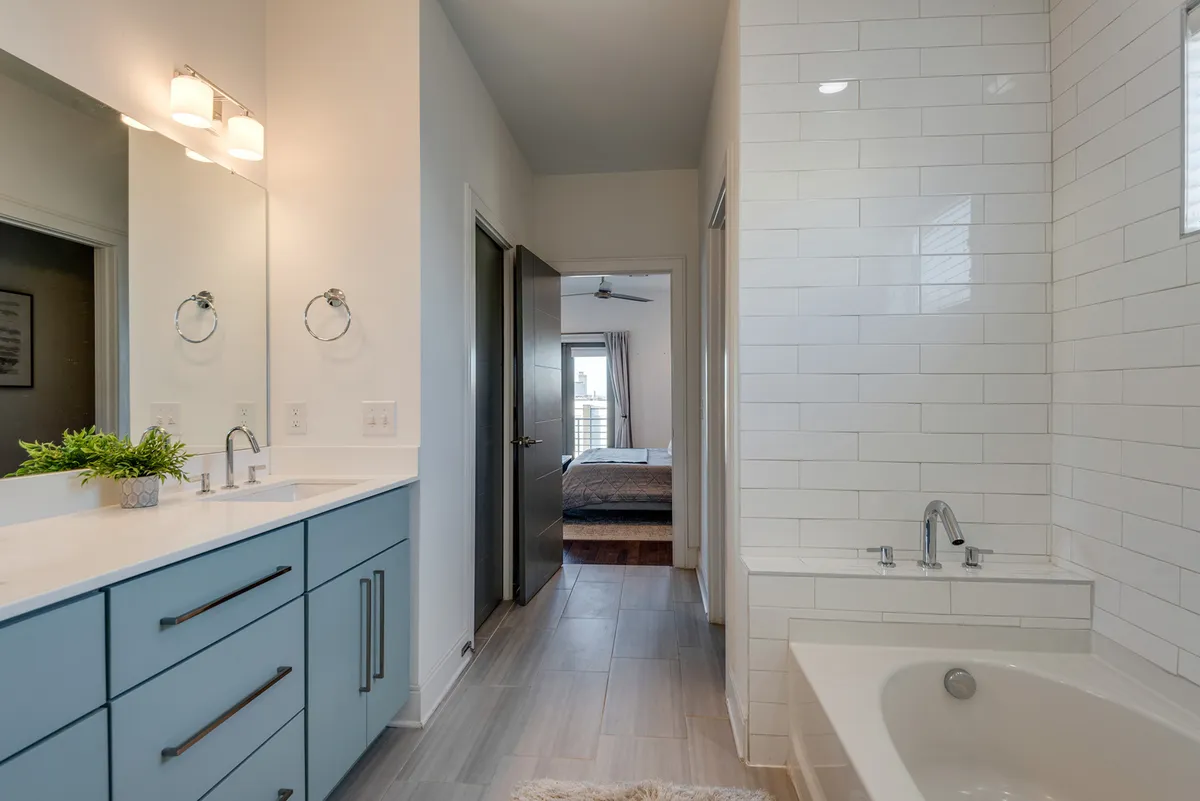 This peaceful bathroom scene features a vanity with sink, bathtub, and a mirror reflecting the adjacent bedroom, subtly connecting the bathroom with the private sleeping quarters.