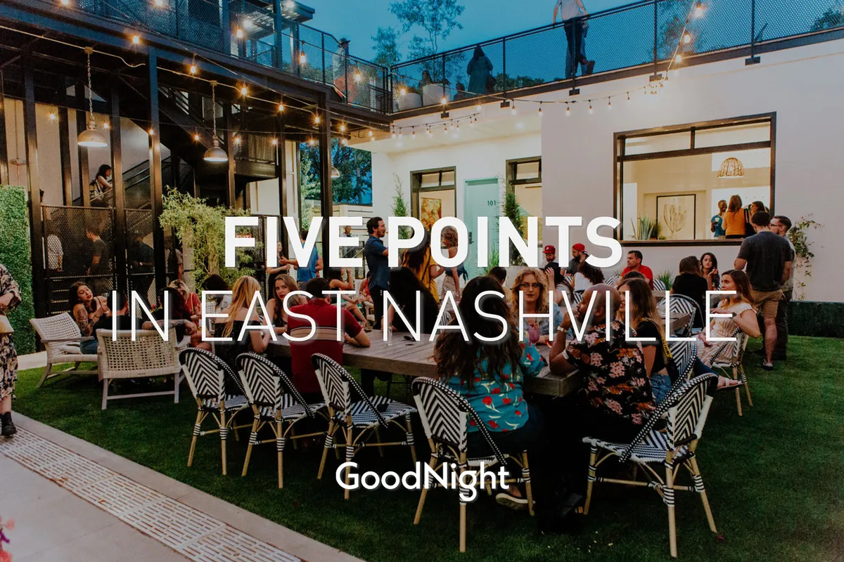 An inviting outdoor dining scene, this image captures a large group of people enjoying a meal together around a festively lit table, with string lights creating a warm, celebratory mood. The lush outdoor setting suggests communal enjoyment and togetherness after a day out.