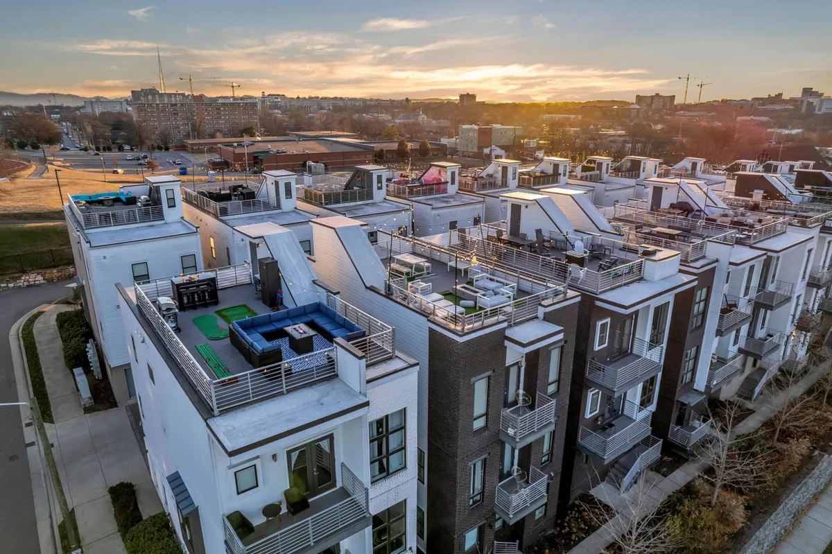 A modern rooftop terrace featuring comfortable outdoor seating and stylish architecture, surrounded by a sweeping cityscape and illuminated by the warm glow of a sunset. The terrace is set up for social gatherings, providing plenty of space for groups to relax, network, or collaborate while enjoying urban views.