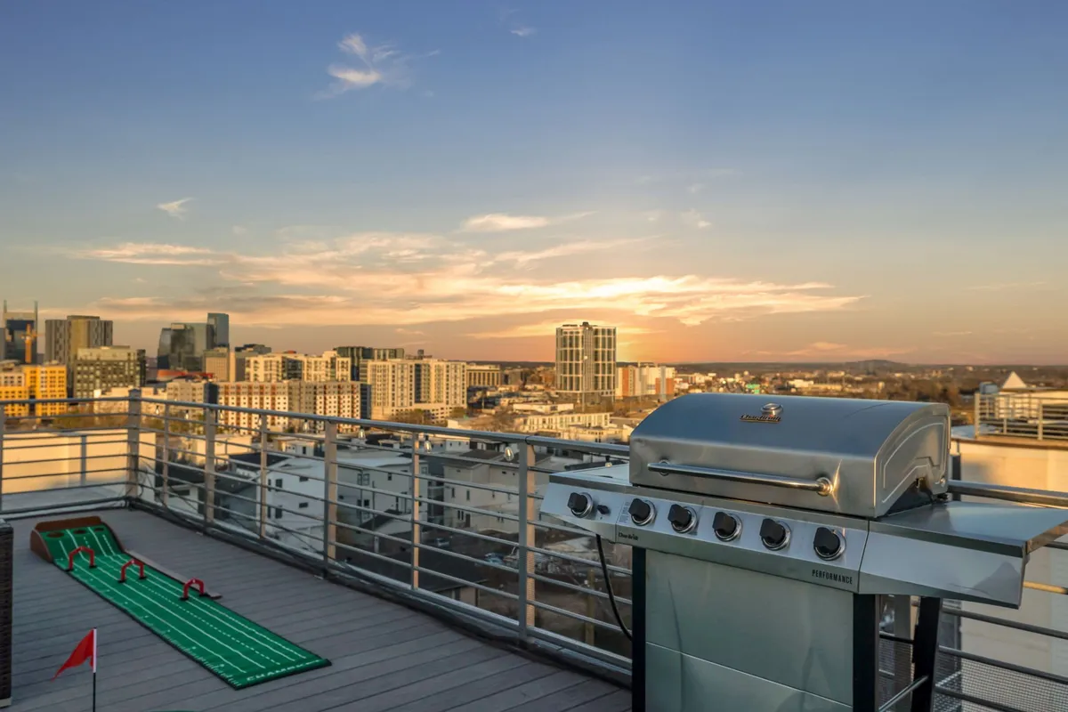 A vibrant scene showing a rooftop grill area adjacent to a mini-golf course, overlooking the city skyline at dusk. Friends gather around the grill and playing green, enjoying food and friendly competition as the city’s lights come alive.