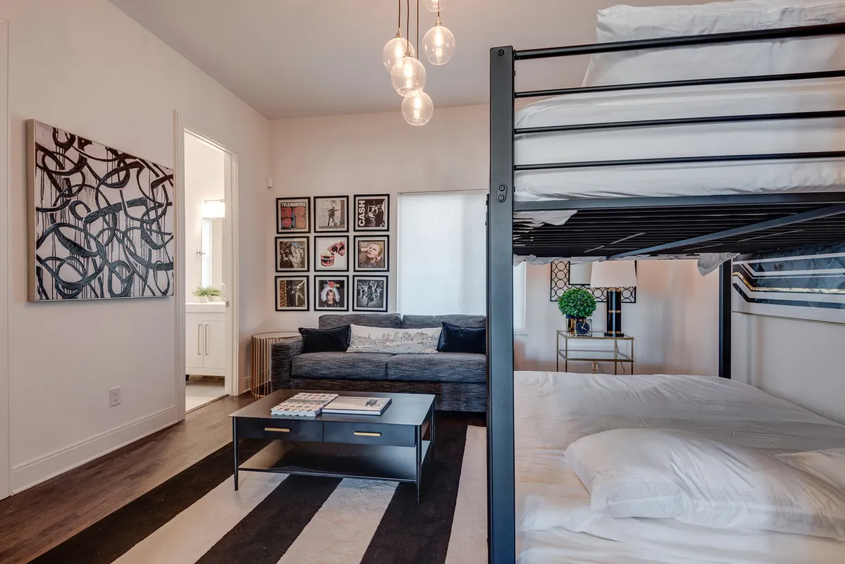 A contemporary bedroom featuring a playful bunk bed, sofa, wall artwork, and a coffee table. The space is lively and practical, ideal for families or groups seeking flexible sleeping arrangements.