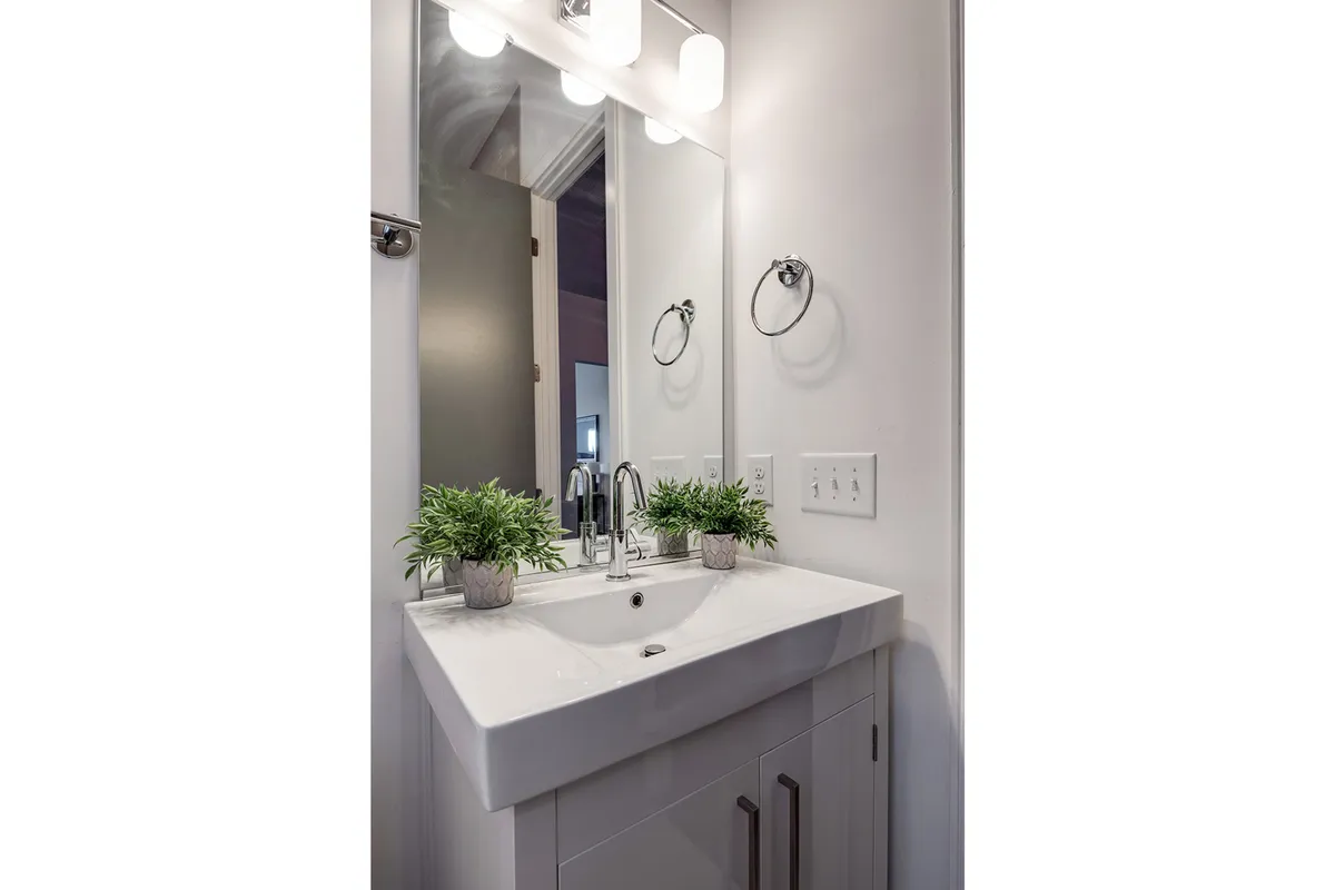 A fresh, inviting bathroom with a modern sink, mirror, stylish light fixtures, and touches of greenery. The setup conveys a feeling of cleanliness and thoughtful amenities.